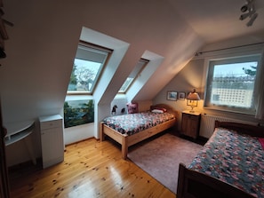 Ein Schlafzimmer mit schrägen Wänden, Holzboden, einem Bett mit floralem Bettbezug, einem Schreibtisch und einer Heizung.