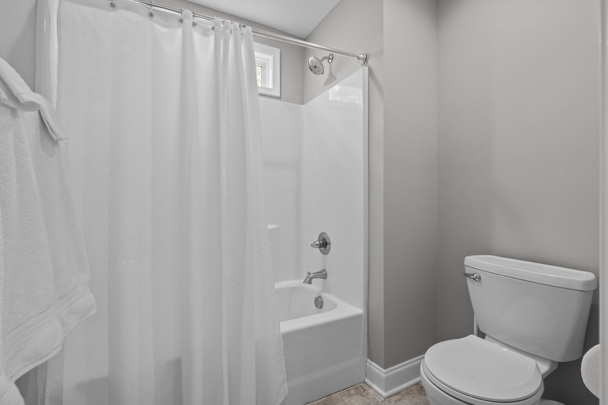 Ein Badezimmer mit Dusche, Toilette und kleinem Fenster.