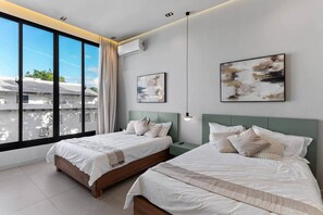 Een moderne hotelkamer met twee bedden, grote ramen en kunstwerken aan de muur.