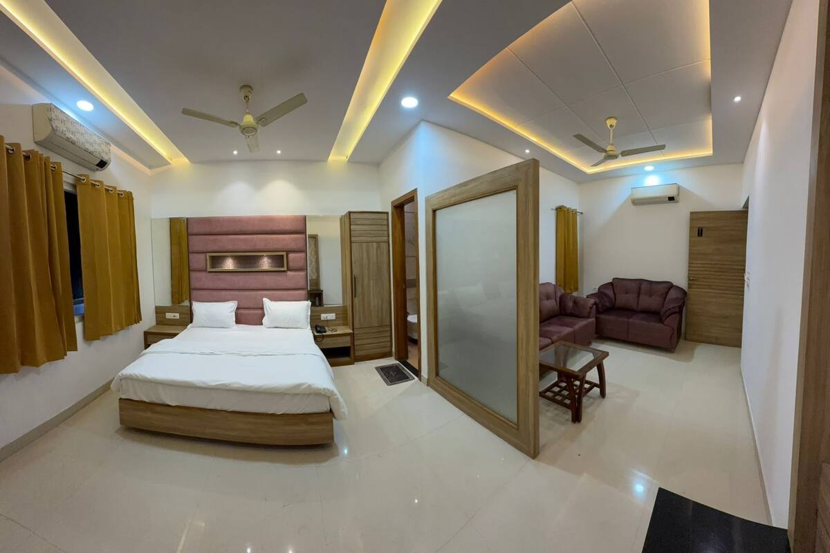 A modern hotel room with a large bed, a sofa, a mirror, and ceiling fans.