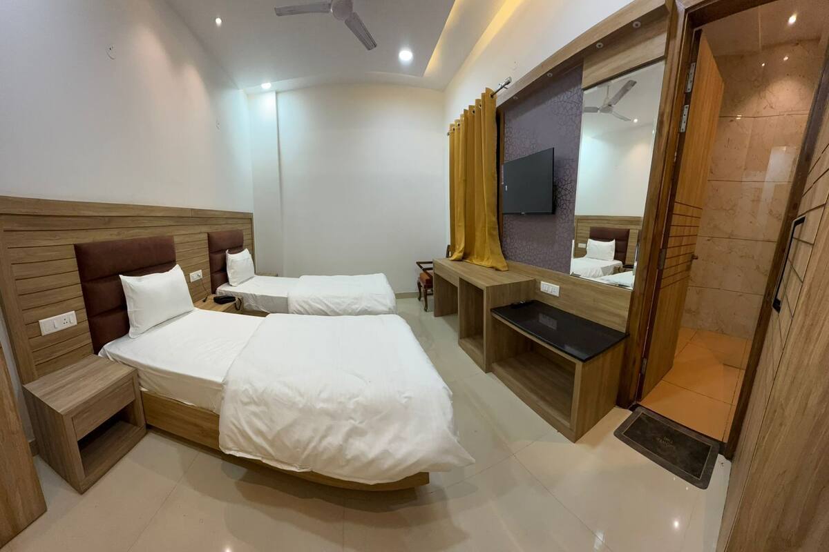 A hotel room with two beds, a TV, a mirror, and a wooden desk.