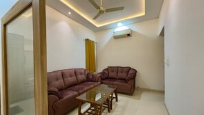 A living room with a sectional sofa, a glass coffee table, and a ceiling fan. - Hotel Silver Bricks (Amritsar)