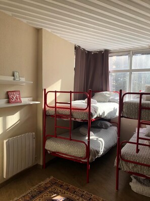 A dormitory room with bunk beds, a radiator, a shelf with books, and a window with curtains. - Warm Sierra Nevada Apartment for 8 (Monachil)