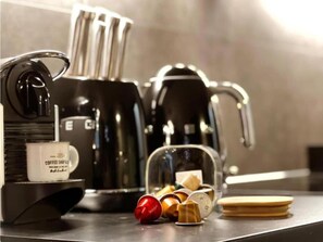 Une machine à café, une cafetière, une tasse et un bocal en verre contenant des capsules de café, le tout posé sur un plan de travail.