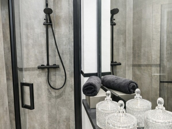 Un bagno moderno con box doccia in vetro, portasciugamani e contenitori trasparenti sul lavabo.