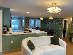 A modern kitchen with a central island, a dining area with wooden chairs, and a large window offering a view. - Skaneateles country home just a short walk to downtown  (Skaneateles)
