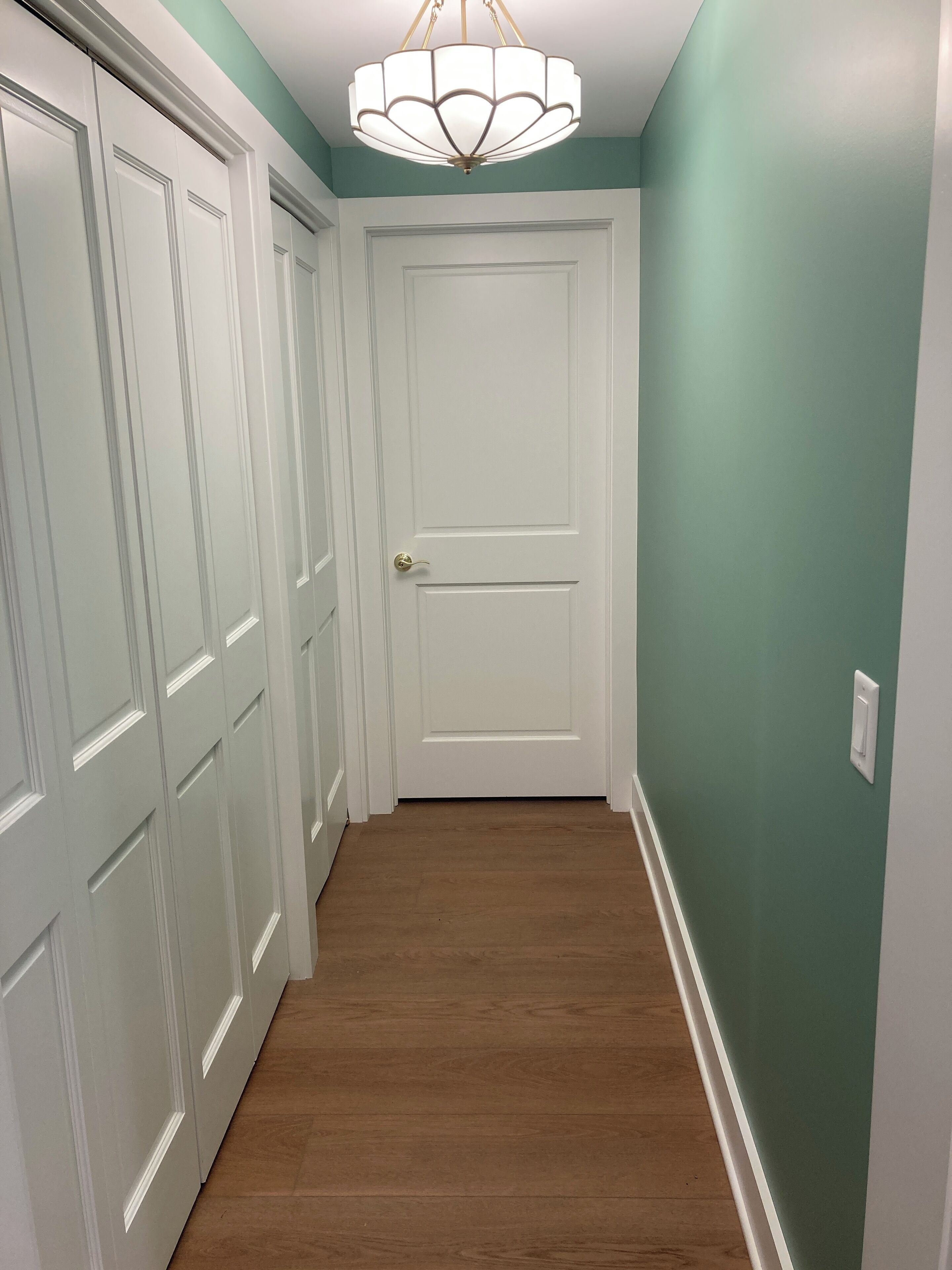 Um corredor com portas brancas, soalho de madeira e parede verde.