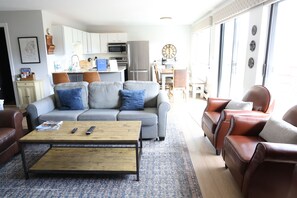 A living room with a sofa, coffee table, and leather armchairs. A kitchen is visible in the background. - Hike in Hike Out at Black Bear View (Silverthorne)