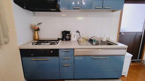 A compact kitchen with blue cabinets, a gas stove, a coffee maker, and a sink.
