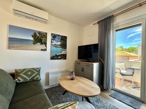 A living room with a sofa, a coffee table, a TV on a cabinet, and a sliding glass door leading to an outdoor area. - Cozy Apartment Silke with Sea view (Krk)