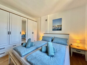 A double bed with matching pillows and a nightstand with a lamp, a wardrobe, and a framed picture on the wall. - Cozy Apartment Silke with Sea view (Krk)