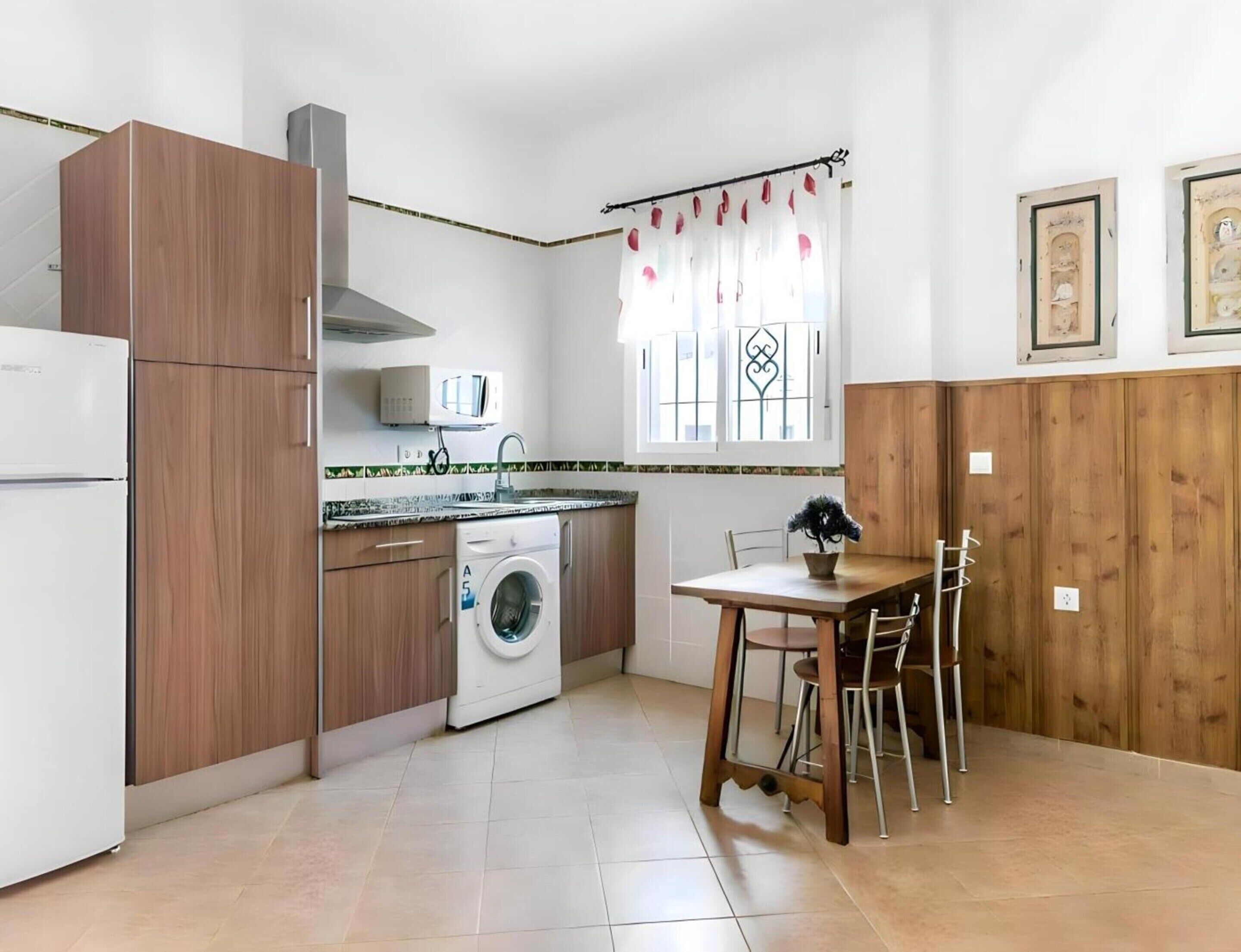 Une cuisine compacte équipée d’un lave-linge, d’un four à micro-ondes et d’un coin repas avec une table et des chaises.