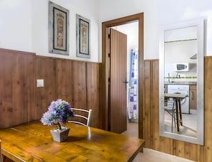 A dining area with a wooden table and chairs, a potted plant, and a view into a kitchen area with a washing machine and microwave. - Peaceful Apartment Close to the Coast (Conil de la Frontera)