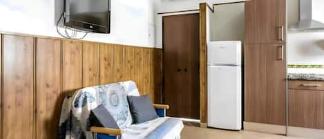 A compact room with a bed, a sofa, a television, a refrigerator, and wooden cabinets.