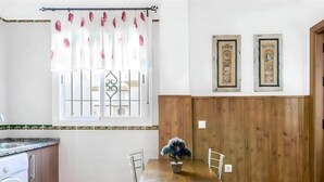 A compact kitchen with a dining table, a washing machine, and a window with decorative curtains. - Peaceful Apartment Close to the Coast (Conil de la Frontera)