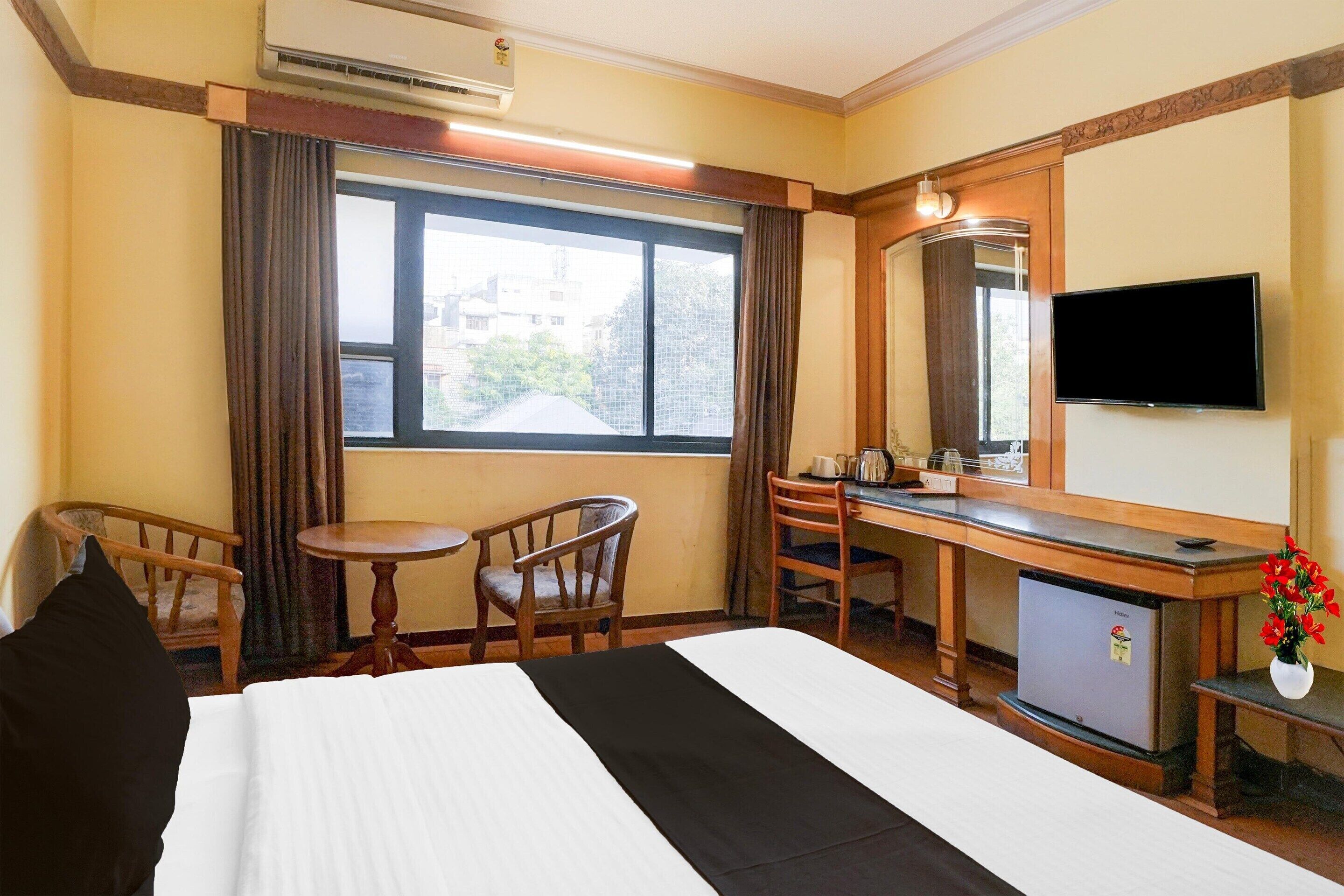 Quarto de hotel com cama, escrivaninha, cadeira, mesa pequena, televisão e frigorífico.