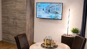 A dining area with a round table, two chairs, a TV mounted on the wall, and a cabinet. - Corner view Residence | Panorama balcony (Koblenz)