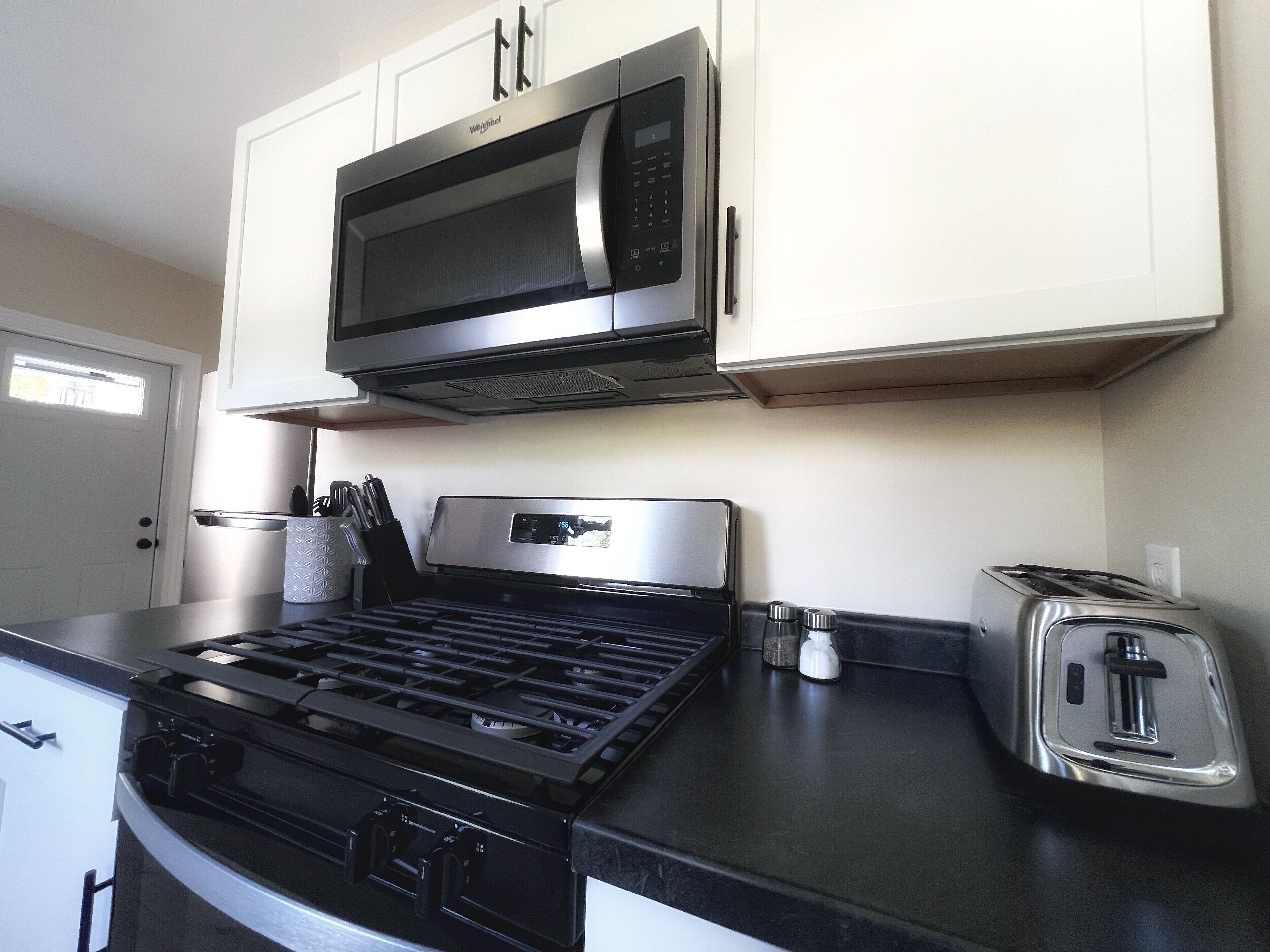 A kitchen with a stove, microwave, toaster, and white cabinets.