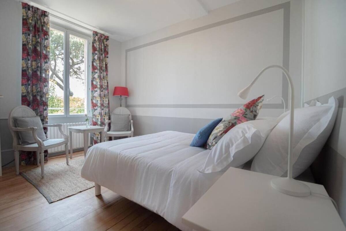 A bedroom with a bed, a chair, a small table, and a window with curtains.
