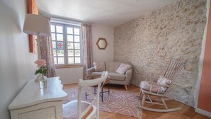 Una habitación acogedora con pared de piedra, un escritorio blanco, una mecedora y un sofá con cojines.