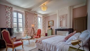 Un dormitorio con cama, una silla, un escritorio, un aparador y una ventana con cortinas.