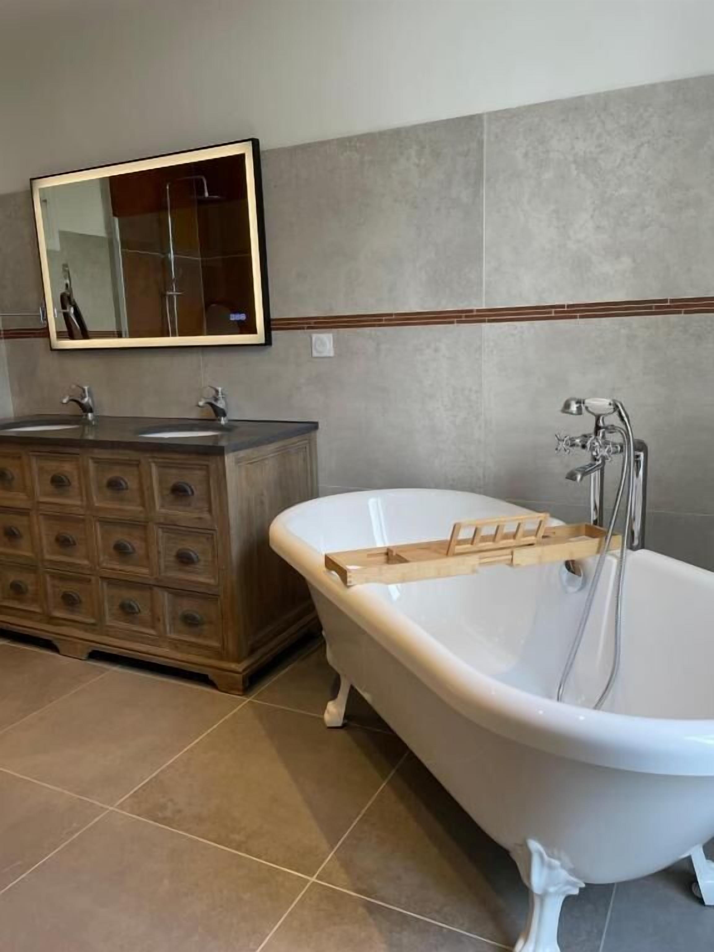 Un baño con una bañera independiente, un lavabo doble con espejo y suelo de baldosas.