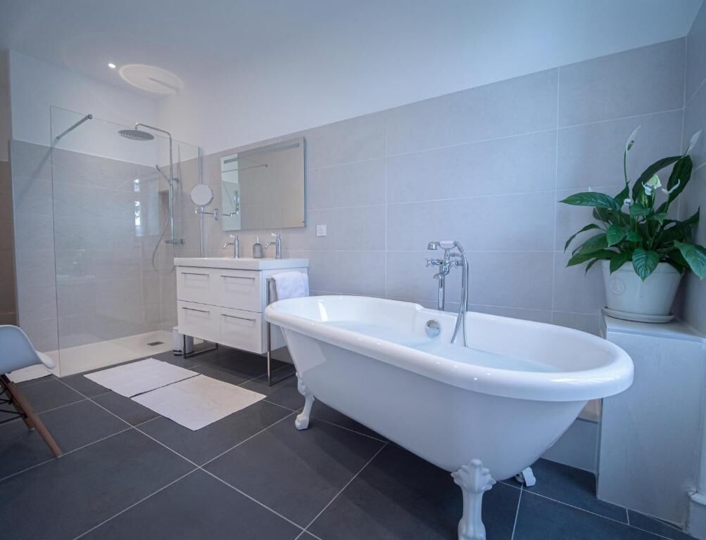 A modern bathroom with a freestanding bathtub, a glass-enclosed shower, a vanity with a mirror, and a potted plant.