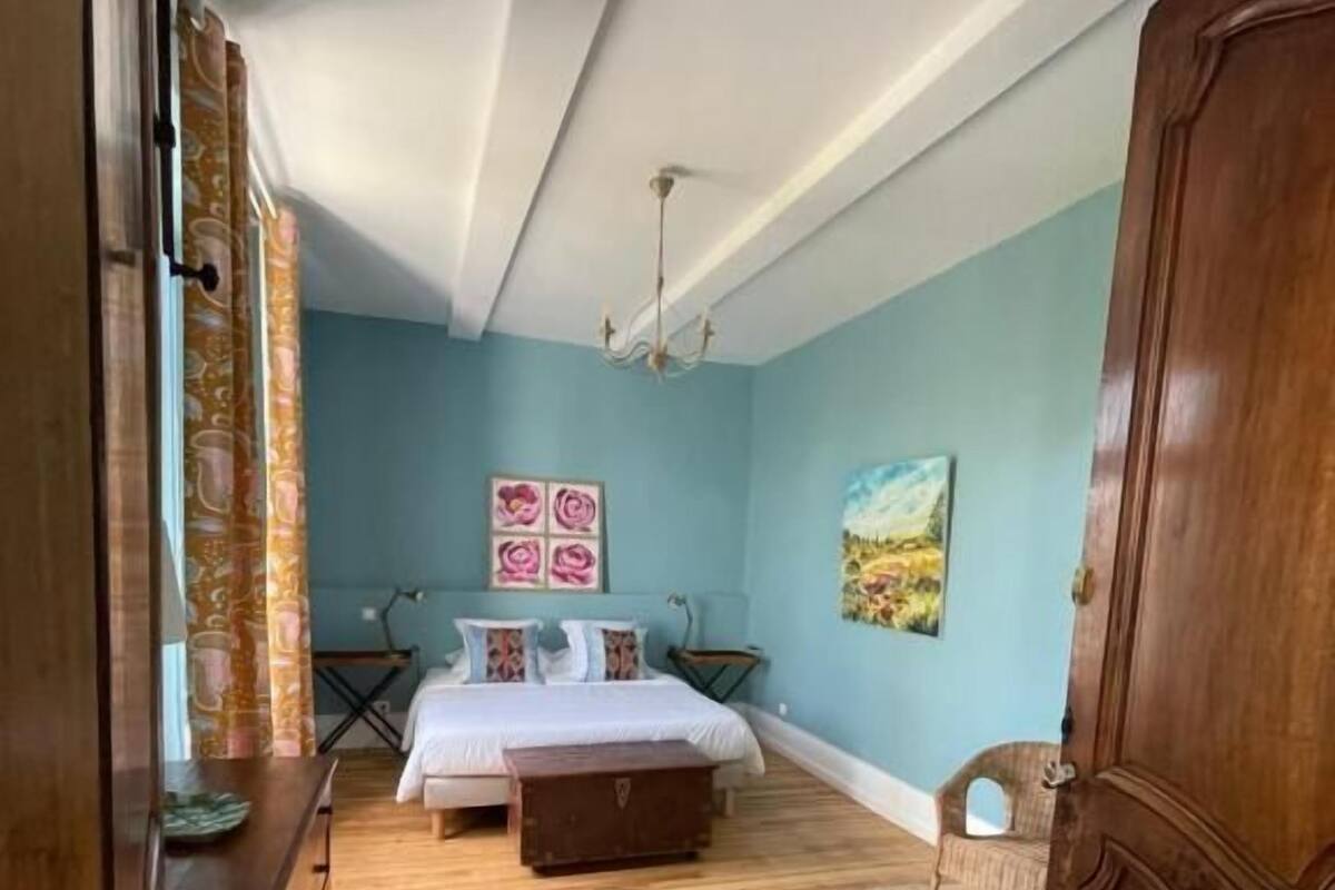 A bedroom with a bed, a wooden dresser, a rug, and a painting on the wall.