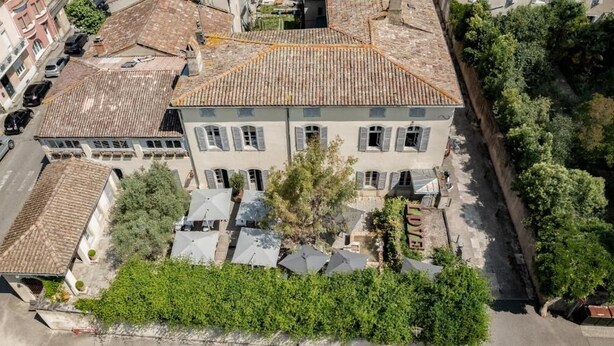 Un edificio de dos pisos con techo de tejas, un patio central y vegetación circundante.