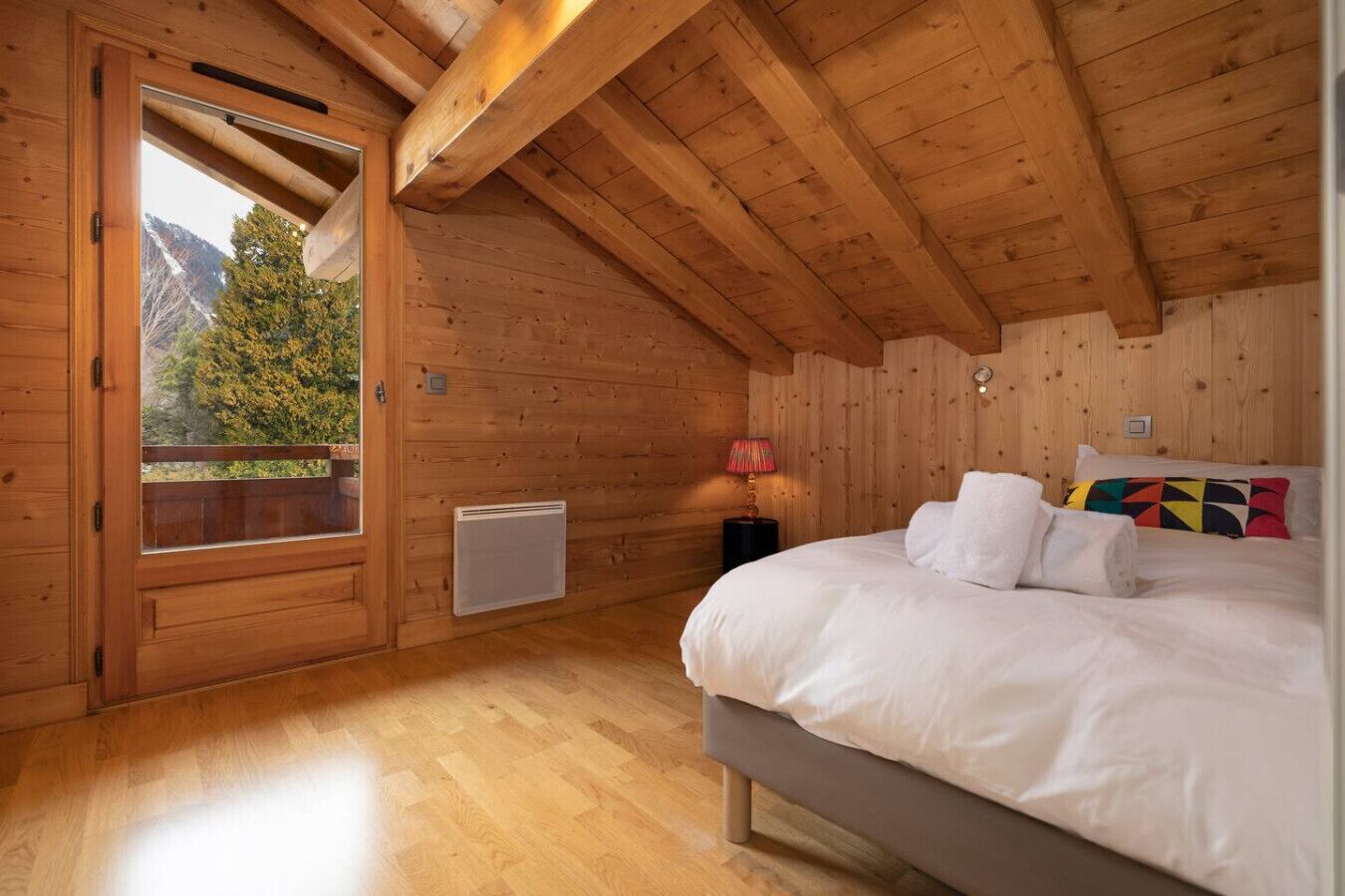 Une chambre dans une cabane en bois, avec un lit, un radiateur, une fenêtre et une vue sur les arbres.
