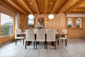 Ein Esszimmer aus Holz mit einem Tisch für sechs Personen, großen Fenstern und Blick ins Freie.