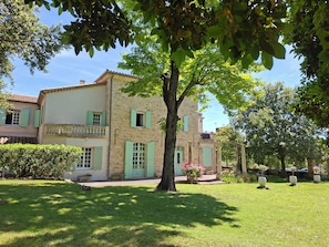 A two-story stone building with green shutters, a balcony, and a well-maintained lawn.
