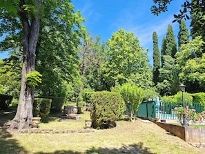 A garden with a variety of trees, a stone structure, and a green fence.