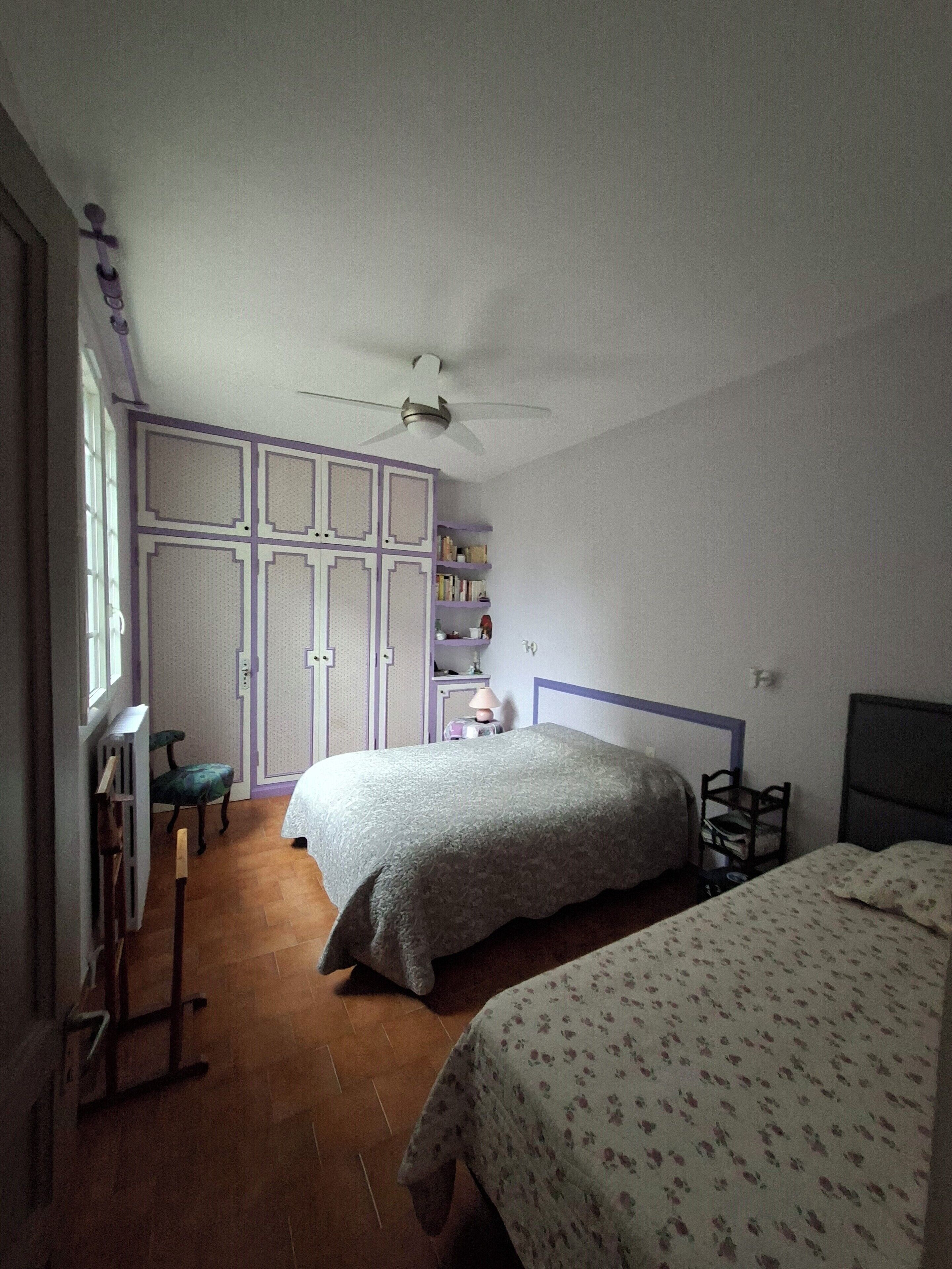 A bedroom with two beds, a ceiling fan, and a wardrobe with a purple frame.