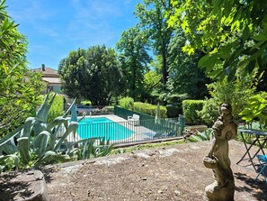 A swimming pool surrounded by greenery, a statue, and a fenced area.