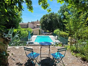 A backyard with a swimming pool, two blue chairs, a table, and a stone sculpture.