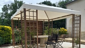 Un espace extérieur abrité, aménagé avec une table et des chaises, entouré de gravier et de verdure.