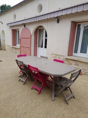 Une table à manger avec des chaises, un mur en pierre et un bâtiment doté de fenêtres en arc de cercle et d’une porte.