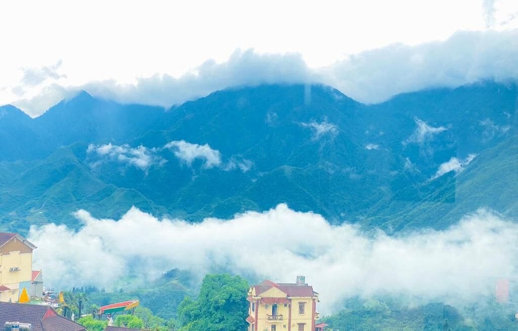 Un paysage montagneux avec des bâtiments situés au pied des montagnes, le tout enveloppé de nuages.