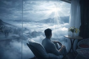 A person seated by a window with a view of a misty landscape and a city below. - Cloud Chaser Hotel (Sa Pa)