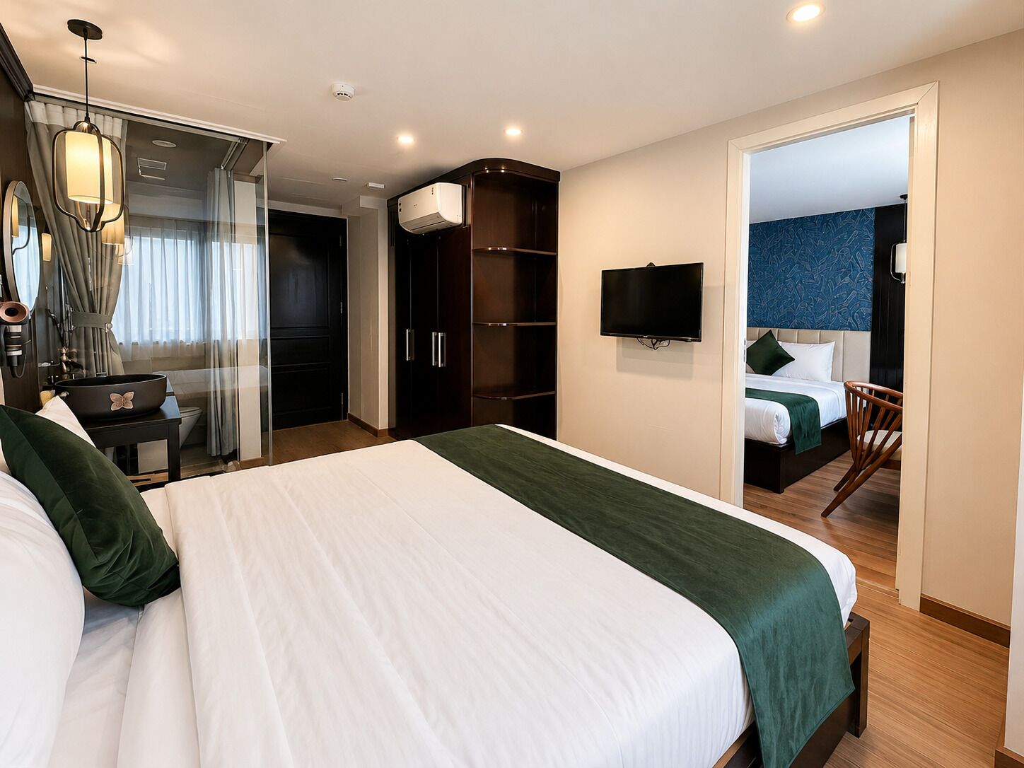 Una habitación de hotel con una cama grande, televisión, armario y baño visible a través de una puerta de cristal.