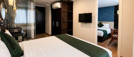 Una habitación de hotel con una cama grande, televisión, armario y baño visible a través de una puerta de cristal.
