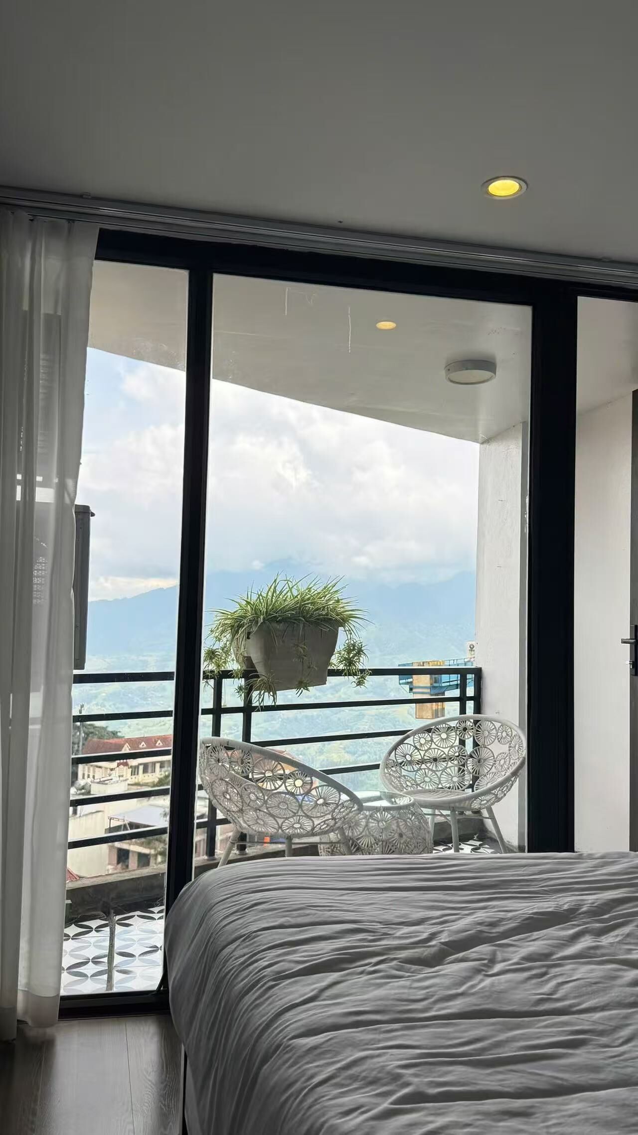 A bedroom with a large bed, a balcony with a hanging plant, and a view of the sea.