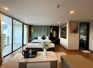 Una habitación de hotel moderna con una cama grande, una mesita de centro, un jarrón con flores, una pequeña mesa con aperitivos y vistas al exterior.