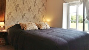 Ein Schlafzimmer mit einem großen Bett, floralem Wandpapier, einem Fenster mit Vorhängen und einem Nachttisch mit Lampe.