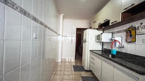 A kitchen with white cabinets, a black countertop, and a refrigerator. - FOR RENT!!! "Apartment in Praia Grande, Canto do Forte" (Praia Grande)