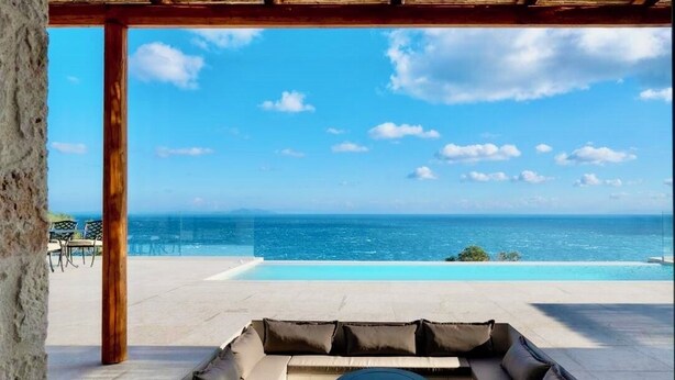 Zona de piscina amb vista a l'oceà, una zona de seients amb coixins i una taula rodona.