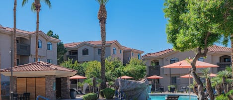 A pool area with lounge chairs, umbrellas, and palm trees.