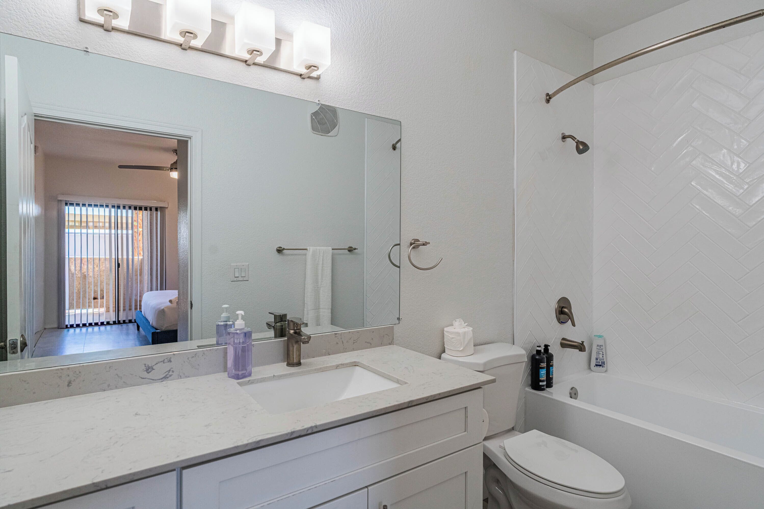 A bathroom with a white sink, mirror, and toilet. There is a shower curtain rod and a towel rack.