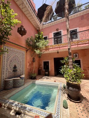 A courtyard with a swimming pool, potted plants, and a decorative wall. - Riad de Charme, 5 minutes Place Jemaa El Fna (Marrakech)
